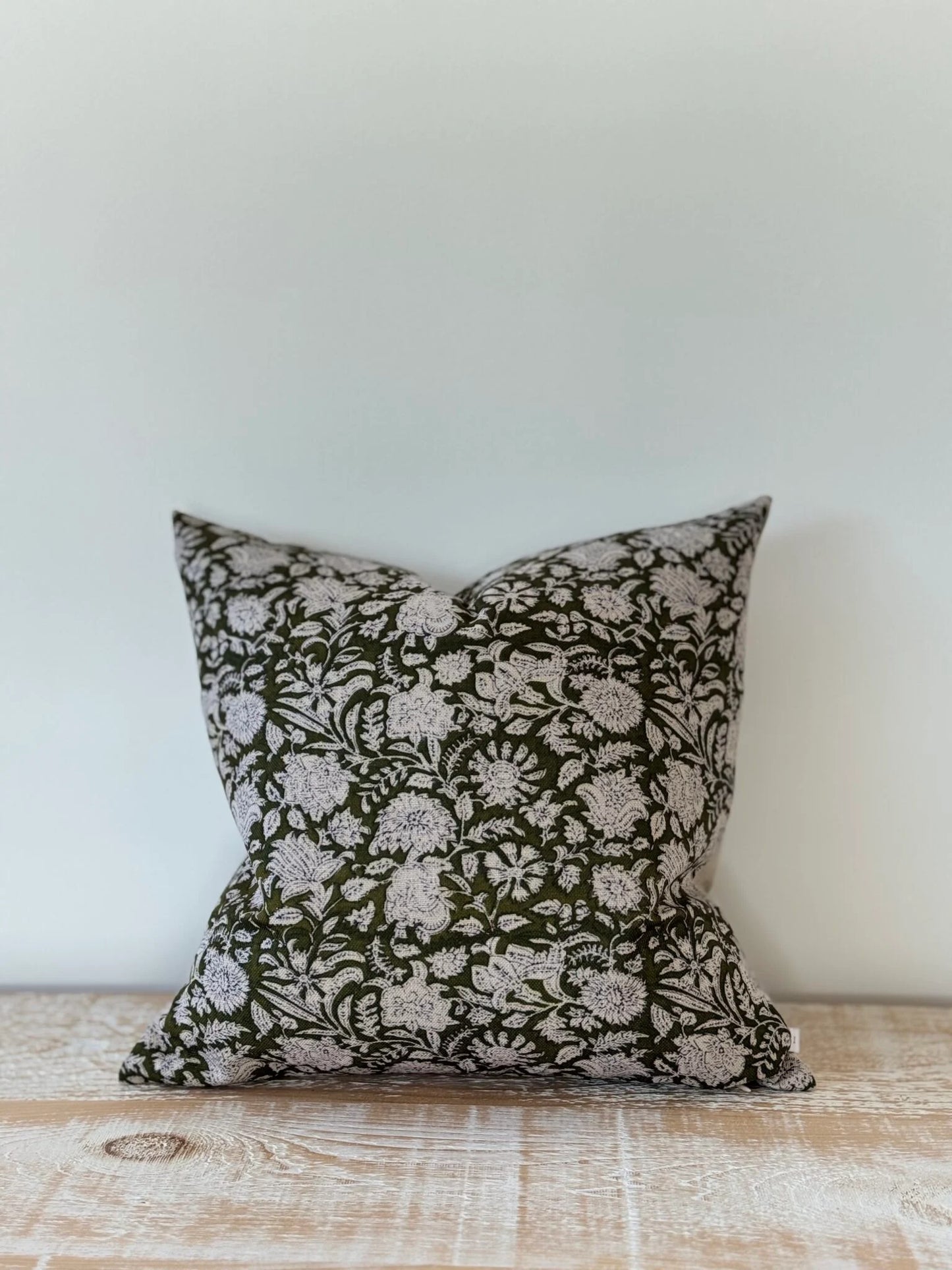 Decorative pillow with floral pattern on a wooden surface against a white wall