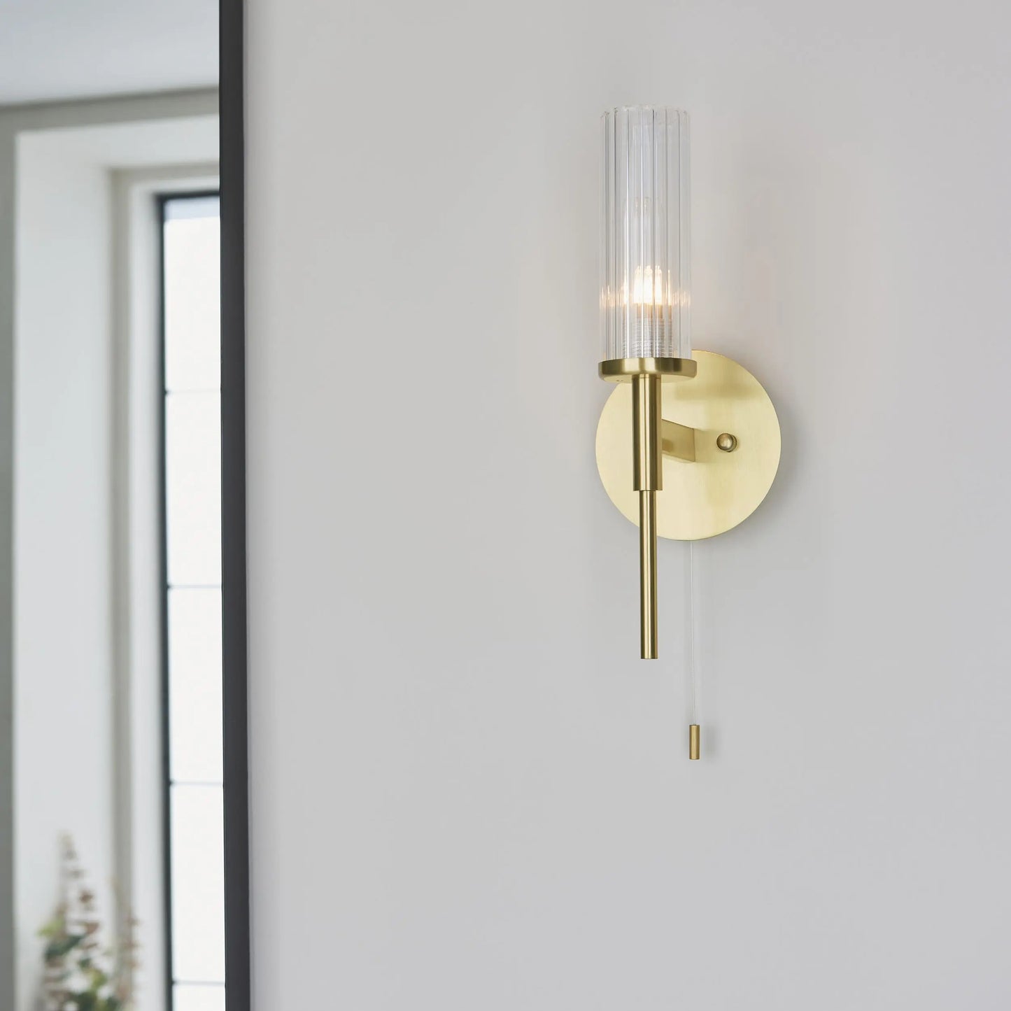 Gold wall sconce with clear glass shade on a light gray wall.