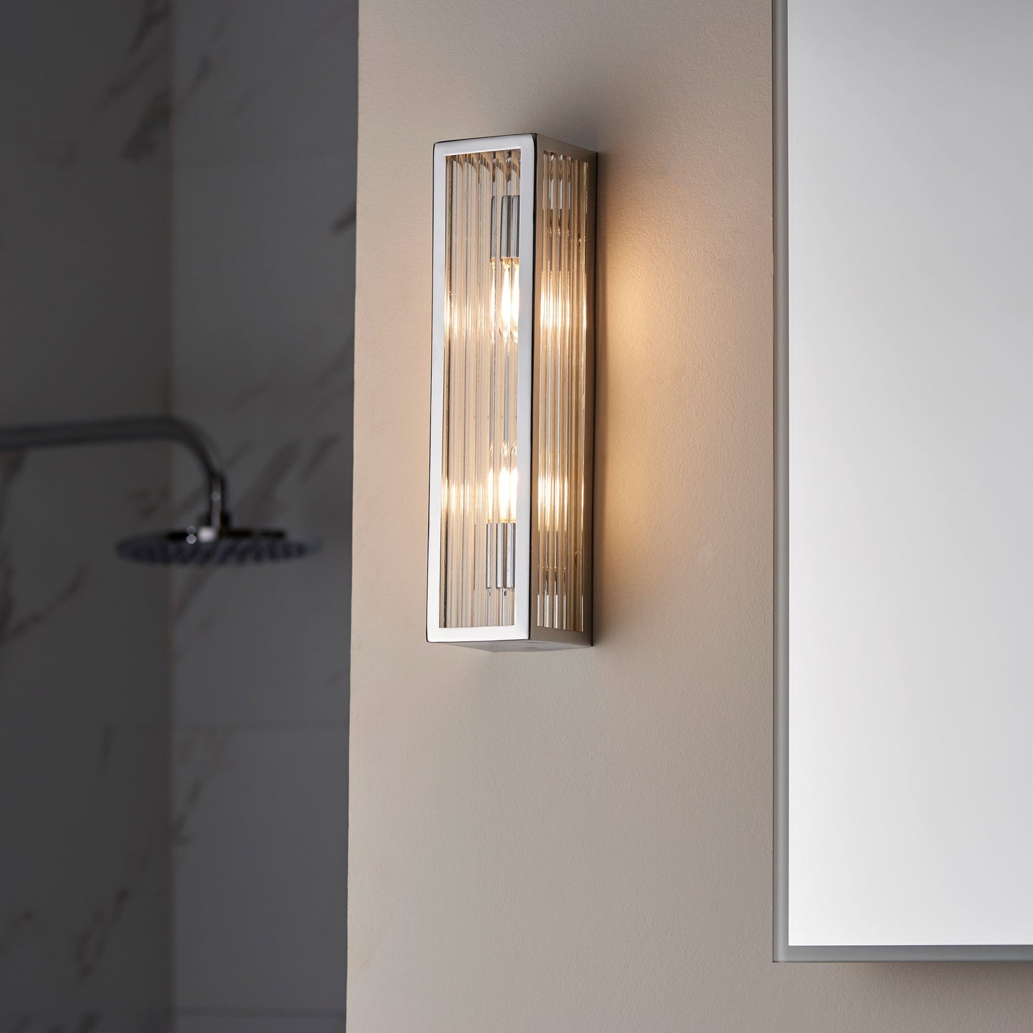 Bathroom wall light fixture with glass panel on a neutral wall.